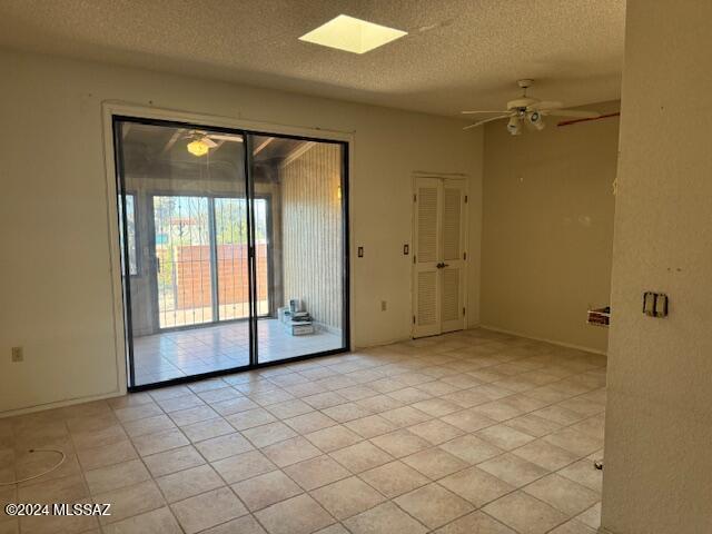 tiled empty room with a textured ceiling, a skylight, and ceiling fan