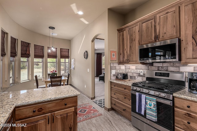 kitchen featuring backsplash, light stone countertops, pendant lighting, and stainless steel appliances