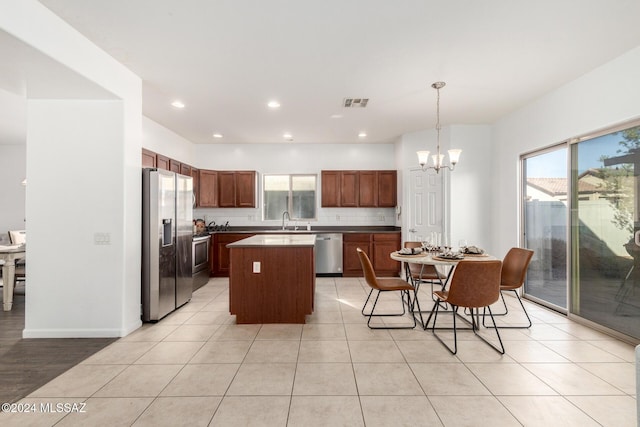 kitchen with sink, hanging light fixtures, appliances with stainless steel finishes, a kitchen island, and a chandelier