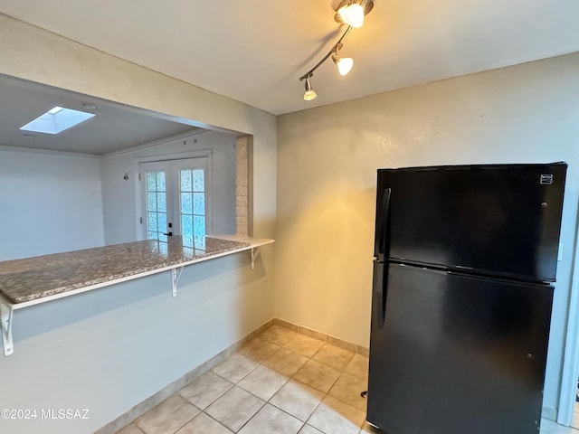 kitchen featuring french doors, black refrigerator, a skylight, light tile patterned floors, and kitchen peninsula