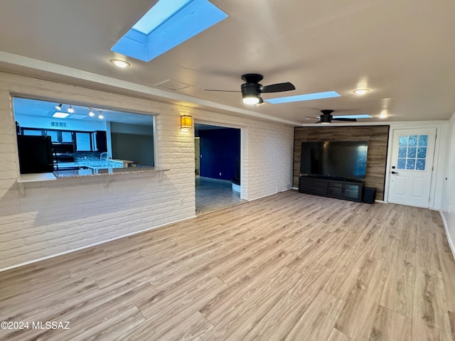 unfurnished living room featuring a skylight, brick wall, ceiling fan, sink, and light hardwood / wood-style flooring