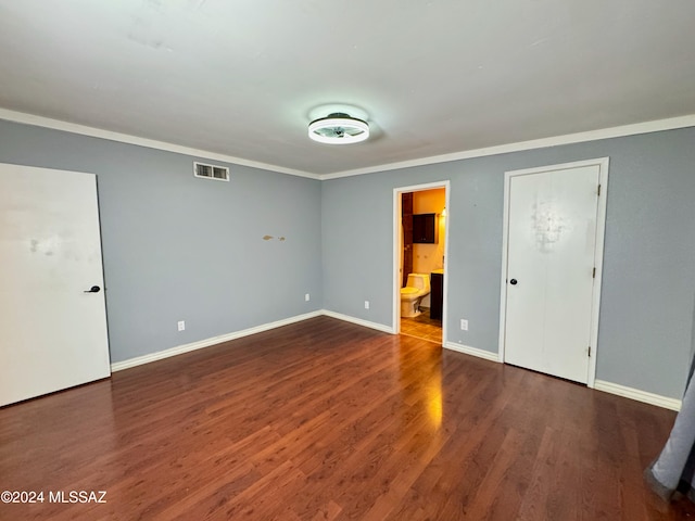 unfurnished bedroom with ensuite bathroom, ornamental molding, and dark wood-type flooring