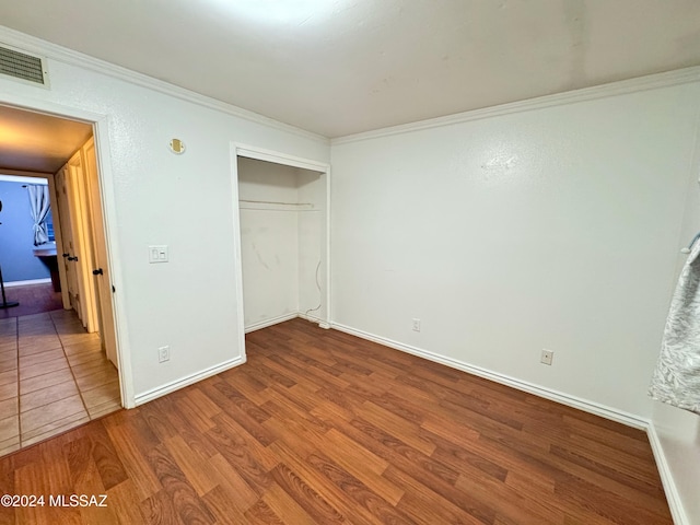 unfurnished bedroom featuring hardwood / wood-style floors, a closet, and crown molding