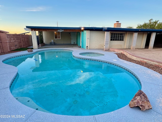 pool at dusk with an in ground hot tub and a patio