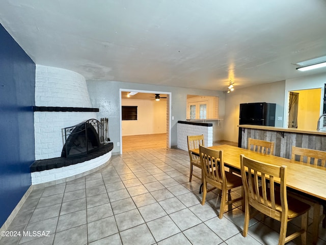 tiled dining area with ceiling fan and a brick fireplace