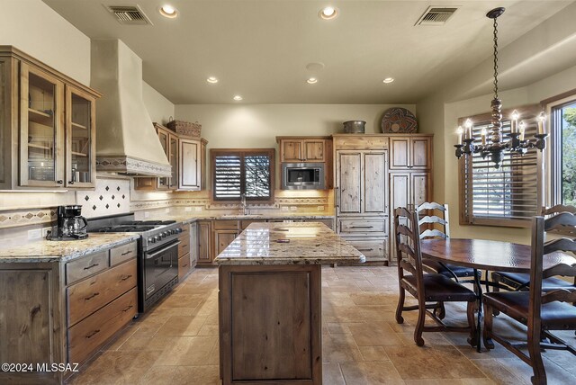 kitchen featuring pendant lighting, wall chimney exhaust hood, light stone countertops, a kitchen island, and stainless steel appliances