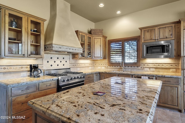 kitchen featuring light stone countertops, sink, stainless steel appliances, and custom range hood