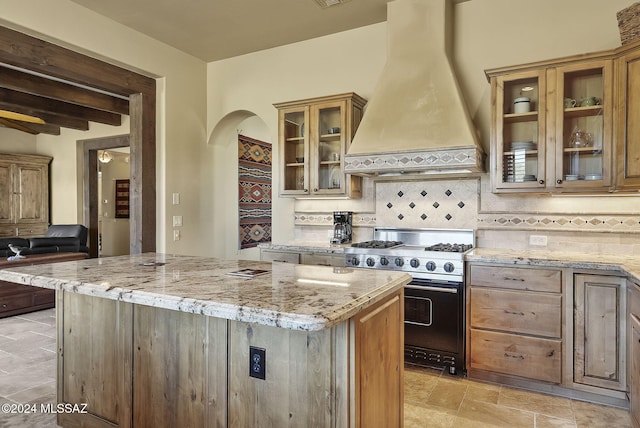 kitchen featuring light stone countertops, a center island, tasteful backsplash, premium stove, and custom exhaust hood