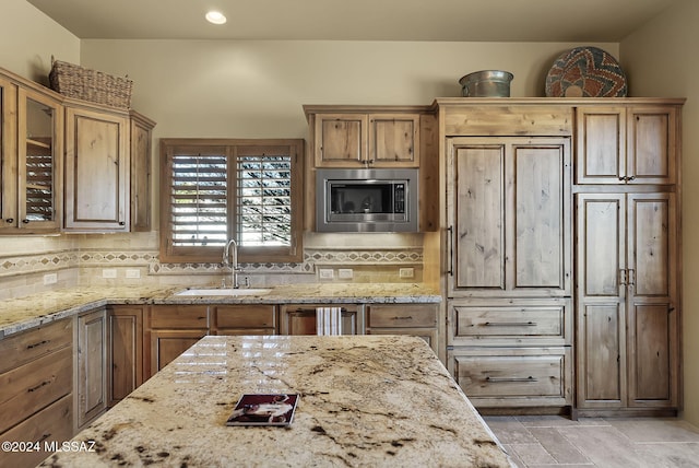 kitchen with stainless steel microwave, backsplash, light stone countertops, and sink