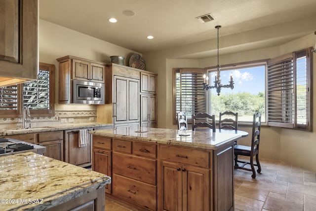 kitchen with stainless steel microwave, sink, a notable chandelier, a kitchen island, and hanging light fixtures