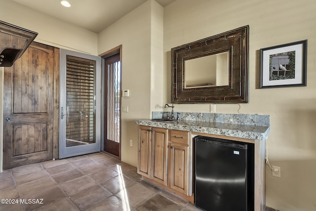 bar with light stone counters, black fridge, and sink