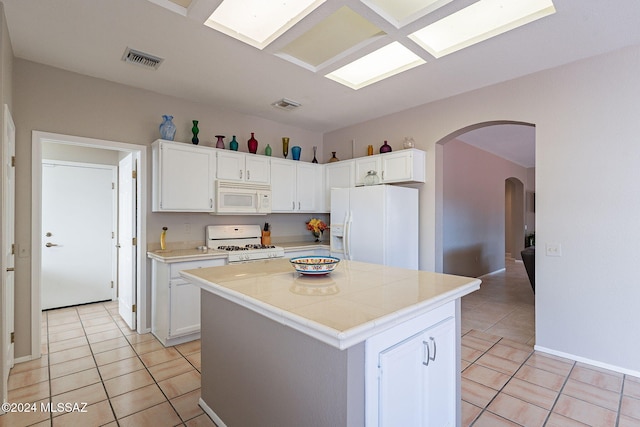 kitchen featuring white cabinets, a center island, white appliances, and light tile patterned floors