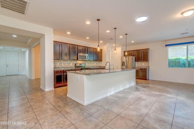 kitchen with decorative light fixtures, light stone counters, stainless steel appliances, and an island with sink