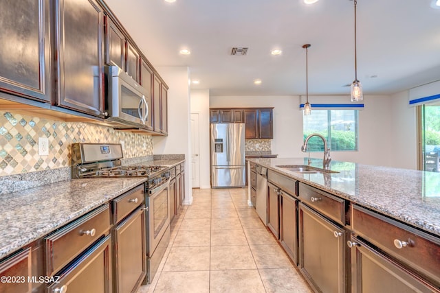 kitchen featuring pendant lighting, appliances with stainless steel finishes, sink, backsplash, and light stone counters