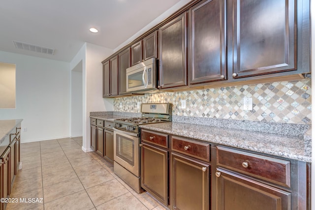 kitchen featuring dark brown cabinetry, stainless steel appliances, tasteful backsplash, light stone counters, and light tile patterned floors