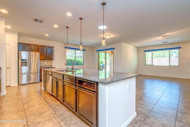 kitchen with hanging light fixtures, a kitchen island with sink, decorative backsplash, sink, and stainless steel appliances