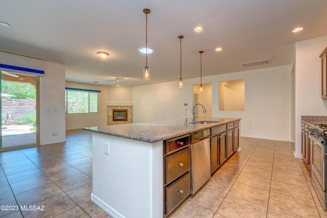 kitchen featuring hanging light fixtures, appliances with stainless steel finishes, sink, light stone countertops, and a center island with sink