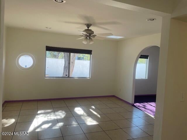 empty room with ceiling fan, light tile patterned flooring, and a healthy amount of sunlight