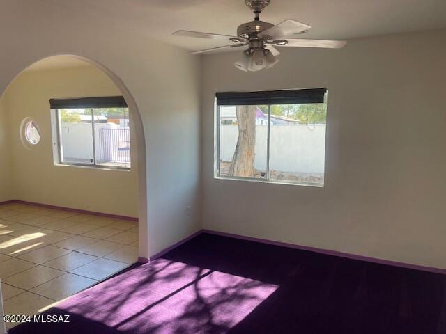 empty room with a wealth of natural light, light tile patterned floors, and ceiling fan