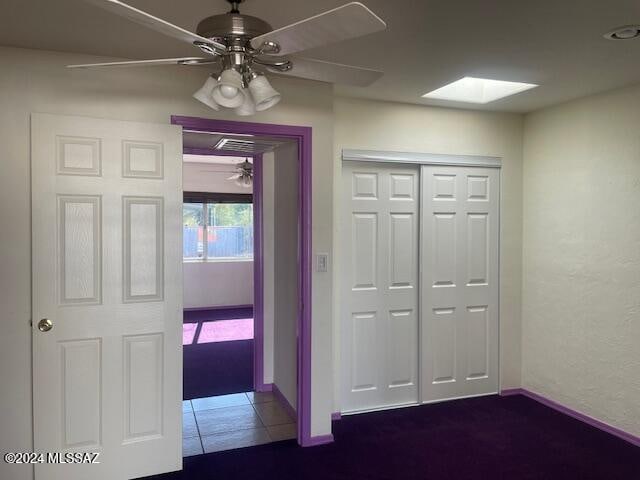 interior space with tile patterned floors, ceiling fan, a skylight, and a closet