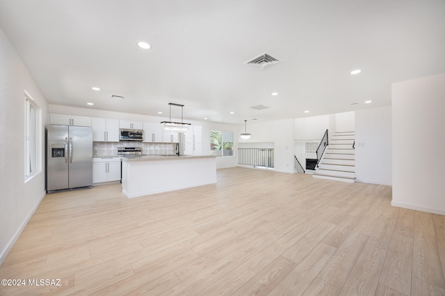 kitchen featuring a center island, hanging light fixtures, light wood-type flooring, appliances with stainless steel finishes, and white cabinetry