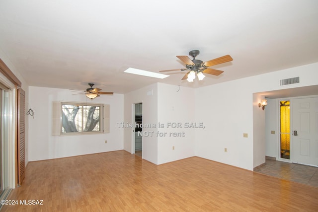 spare room with ceiling fan, a skylight, wood finished floors, and visible vents