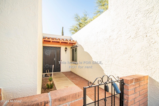 entrance to property with a tiled roof, a gate, and stucco siding