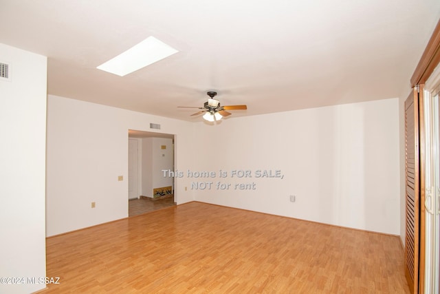 unfurnished room featuring light wood finished floors, a skylight, and visible vents