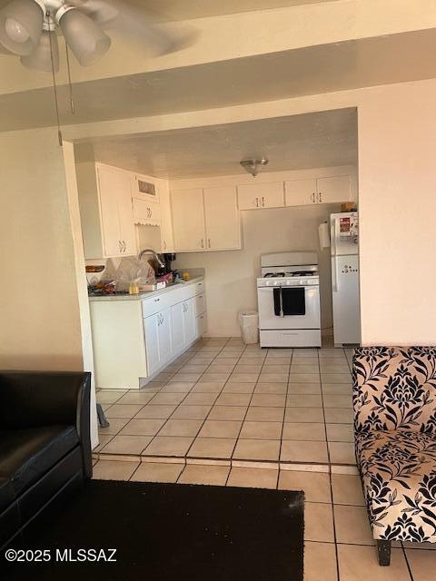 kitchen with white appliances, sink, ceiling fan, light tile patterned floors, and white cabinetry