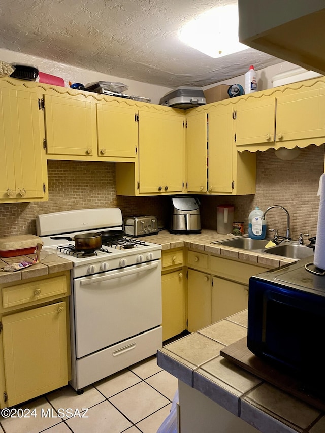 kitchen featuring white gas range, tile counters, and sink