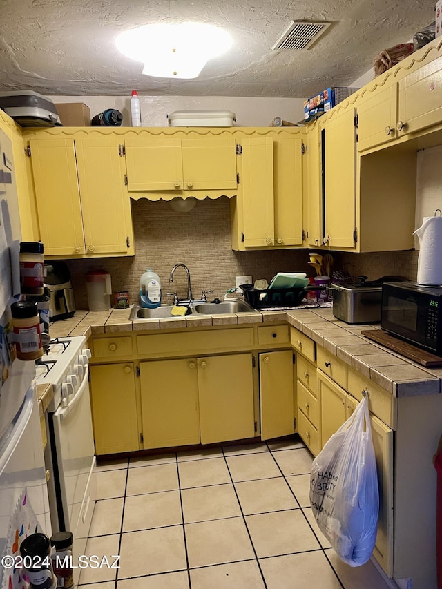 kitchen featuring tile countertops, white gas range oven, sink, light tile patterned floors, and a textured ceiling