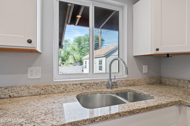 kitchen with white cabinets, light stone counters, and sink