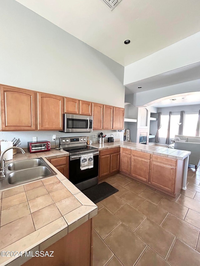 kitchen with kitchen peninsula, tile counters, sink, and stainless steel appliances