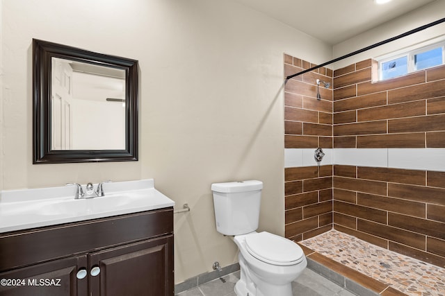 bathroom with tile patterned flooring, vanity, toilet, and tiled shower