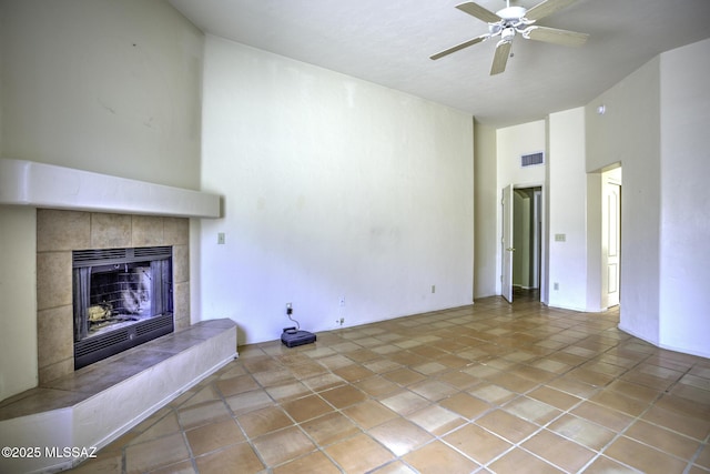 unfurnished living room featuring ceiling fan, a towering ceiling, light tile patterned flooring, and a fireplace