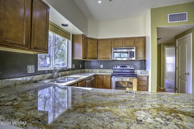 kitchen with stainless steel appliances, light stone countertops, and sink