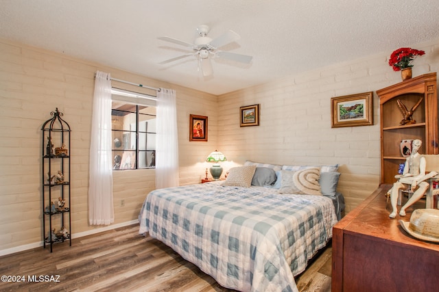 bedroom featuring a textured ceiling, hardwood / wood-style flooring, ceiling fan, and brick wall