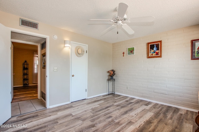 unfurnished room featuring ceiling fan, light hardwood / wood-style flooring, brick wall, and a textured ceiling