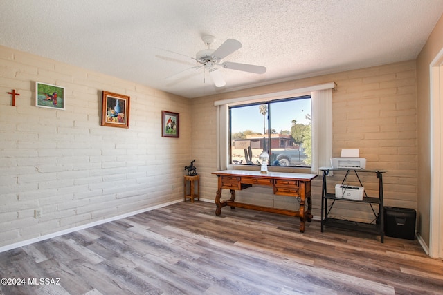 home office with wood-type flooring, a textured ceiling, ceiling fan, and brick wall