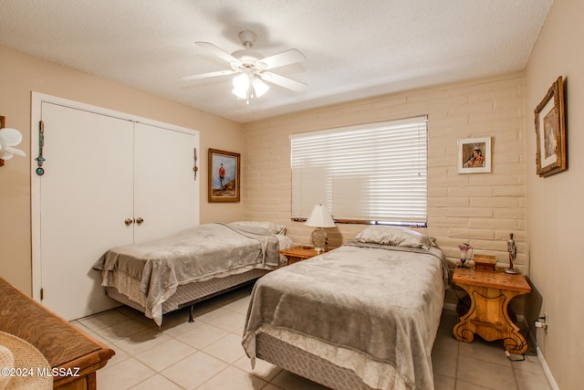 bedroom with ceiling fan, a closet, light tile patterned floors, and a textured ceiling