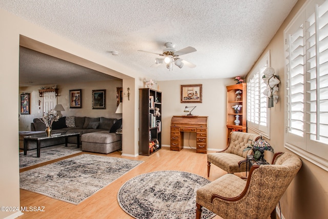 living room with ceiling fan, light hardwood / wood-style floors, and a textured ceiling