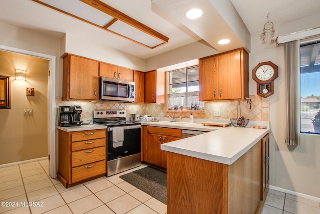 kitchen featuring backsplash, kitchen peninsula, light tile patterned flooring, and appliances with stainless steel finishes