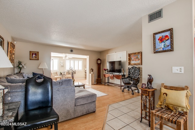 living room featuring a textured ceiling, light wood-type flooring, and ceiling fan