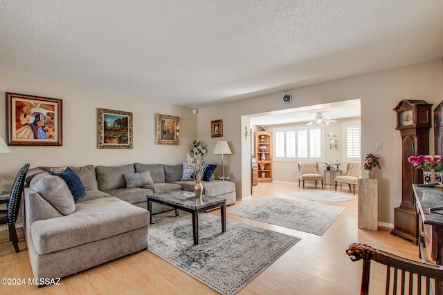 living room featuring ceiling fan, light wood-type flooring, and a textured ceiling