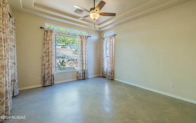 unfurnished room with ceiling fan, a raised ceiling, and concrete flooring