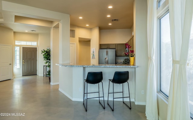 kitchen featuring a wealth of natural light, light stone counters, a kitchen bar, and stainless steel refrigerator