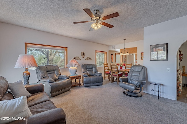 carpeted living room with ceiling fan with notable chandelier and a textured ceiling