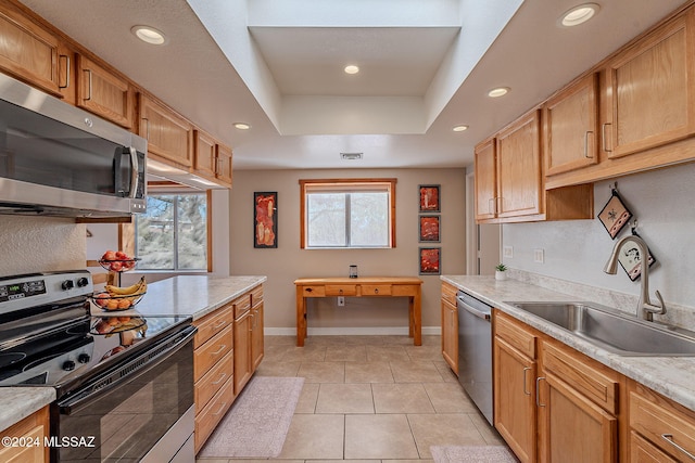 kitchen with appliances with stainless steel finishes, sink, light tile patterned floors, light stone countertops, and a tray ceiling