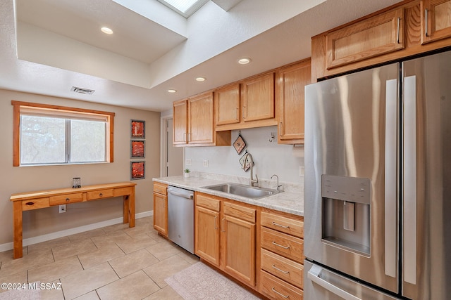 kitchen featuring light stone countertops, a tray ceiling, stainless steel appliances, sink, and light tile patterned floors