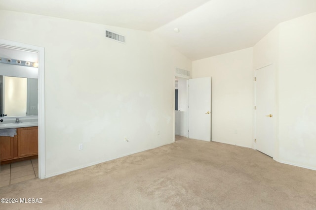 unfurnished bedroom featuring ensuite bathroom, light colored carpet, and lofted ceiling